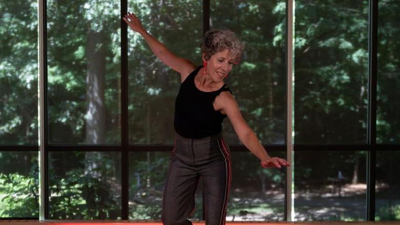 Woman tap dancing in a studio in front of wall of windows